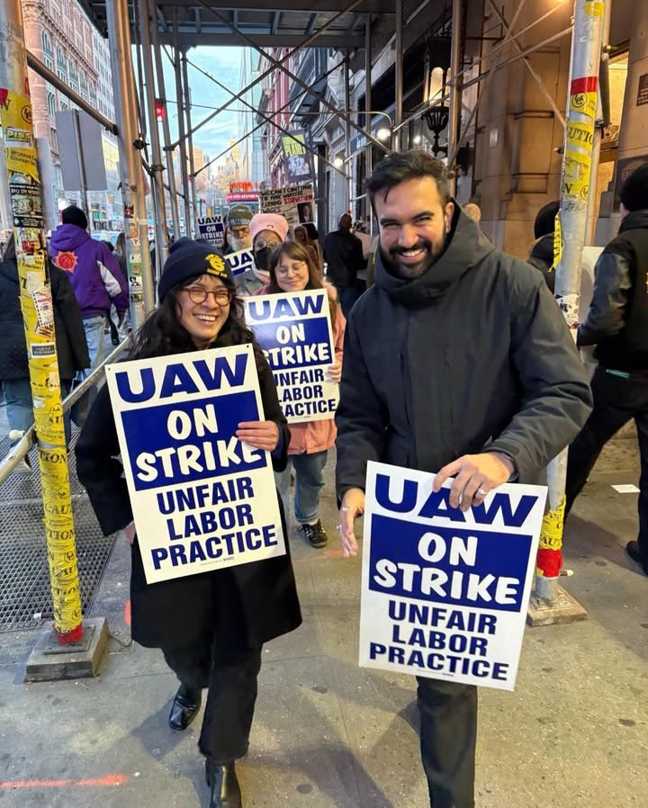 May be an image of standing, poster, banner and text that says 'UTIO UAW ON UAW TRIKE NFAIR ABOR ON ACTICE STRIKE UNFAIR LABOR PRACTICE UAW ON Atm IU STRIKE UNFAIR PRACTICE LABOR'