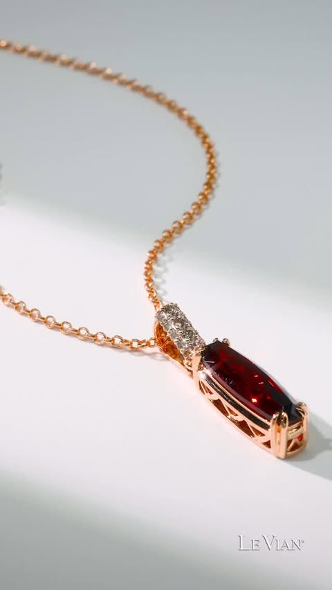 A garnet elongated gemstone necklace set in gold with accents of diamonds at the top. It sits on a white background as the camera moves across it, showing its sparkle and beauty.