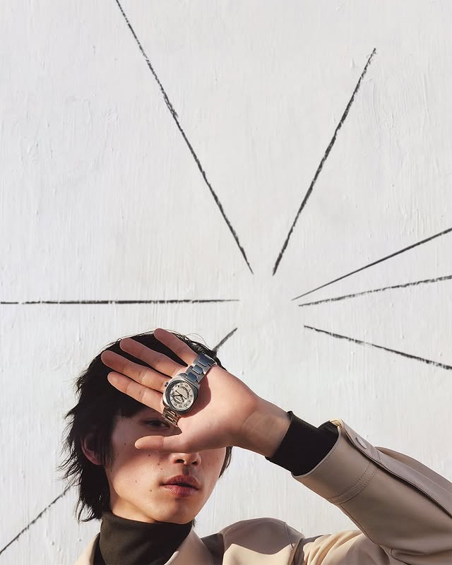 May be an image of duffle coat, wrist watch, overcoat, turtleneck, jacket and bolo tie