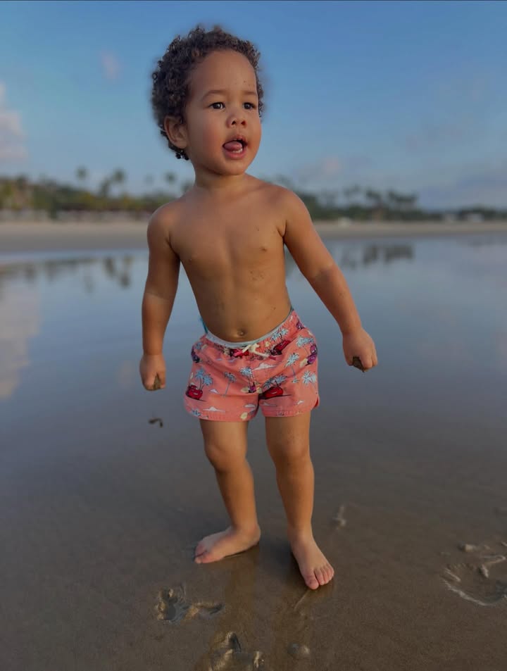 May be an image of baby, standing, beach, ocean and text