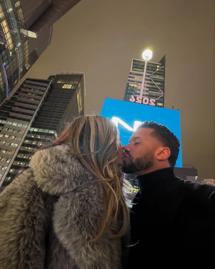 May be an image of one or more people, people kissing, people standing, fur, Times Square, night and text